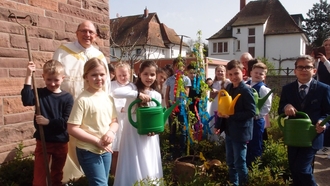 Im Festkleid mit Hacke und Spaten: Die Kommunionkinder pflanzen einen KORNEL-Kirschbaum zum 60. Geburtstag beim Grundstein der Kirche. Gute Früchte auch im Glauben an Jesus.